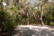 View into sandy site seventeen showing picnic table, wooden railings and electric hookup under shady live oak and maritime hammock in Anastasia State Park.