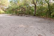 Rear view of sandy site nineteen showing picnic table, fire ring and wooden railings nestled amongst the shady live oak and maritime hammock in Anastasia State Park.