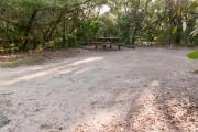 View of sandy site nineteen showing live oak trees, picnic table, fire ring and wooden railings under shady maritime hammock in Anastasia State Park.