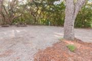 View into sandy site 20 showing picnic table, fire ring, electric and water hookup under shady maritime hammock in Anastasia State Park.