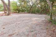 View of sandy site 20 showing live oak trees, picnic table, fire ring and wooden railings under shady maritime hammock in Anastasia State Park.
