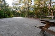 Rear view of sandy site 101 showing picnic table, fire ring, wooden railings and lantern post nestled under the shady live oak trees and maritime hammock in Anastasia State Park