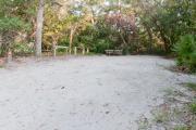 Side view of sandy site 101 showing picnic table, lantern post and wooden railing with live oak trees nestled under shady maritime hammock in Anastasia State Park.
