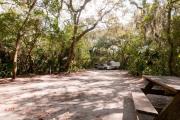 Rear view of sandy site 108 showing picnic table, fire ring, wooden railings and lantern post nestled under the shady live oak trees and maritime hammock in Anastasia State Park.