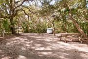 Rear view of sandy site 109 showing picnic table and electric hookup nestled under the shady live oak trees and maritime hammock in Anastasia State Park.
