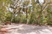Frontal view of sandy site 112 showing picnic table and electric and water hookups with live oak trees nestled under shady maritime hammock in Anastasia State Park.