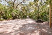 Rear view of sandy site 117 showing picnic table and lantern post nestled under the shady live oak trees and maritime hammock in Anastasia State Park.