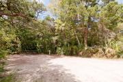 Side view of sandy site 128 showing picnic table and electric and water hookups with live oak trees nestled under shady maritime hammock in Anastasia State Park.