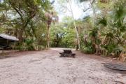 Rear view of sandy site 135 showing picnic table and fire ring nestled under the shady live oak trees and maritime hammock in Anastasia State Park.