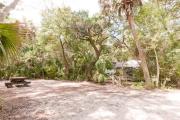 Side view of sandy site 135 showing picnic table and electric and water hookups with live oak trees nestled under shady maritime hammock in Anastasia State Park.