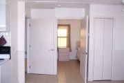 Photo: 002, Interior of cabin, white walls, tan tile floors, open bedroom door straight ahead, stove on left.