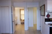 Photo: 003, Interior of cabin, white walls, tan tile floors, 2 open bedroom doors straight ahead, stove on right.