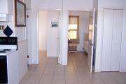 Photo: 004, Interior of cabin, white walls, tan tile floors, 2 open bedroom doors straight ahead, stove on left.