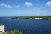 Photo: 006, View from cabin deck, overlooking boating basin with small spit of land, mangroves and open water in the background, white fence on left.