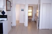 Photo: 006, Interior of cabin, white walls, tan tile floors, 2 open bedroom doors straight ahead, stove on left.
