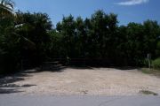 Photo: Buttonwood: Gravel, partially shaded campsite with picnic table and grill, bordered by a wood fence and surrounded by bushes.