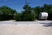Photo: Buttonwood: Paved road with two campsites on the other side, campsite on right has a camper on it, bushes and fences border sites.
