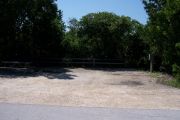 Photo: Buttonwood: Partially shaded gravel campsite with picnic table and grill, bordered by a wood fence and surrounded by bushes.