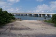Photo: Buttonwood: Gravel site with picnic table and grill, bushes on both sides, water and new Bahia Honda Bridge in the background.
