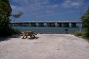 Photo: Buttonwood: Gravel site with picnic table and grill, bushes on either side, water and new Bahia Honda Bridge in the background.