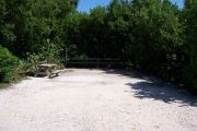 Photo: Buttonwood: Partially shaded gravel campsite with picnic table and grill, bordered by a wood fence and surrounded by bushes and palms.