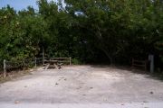 Photo: Buttonwood: Sunny gravel campsite with picnic table and grill bordered by a wood fence and surrounded by bushes.