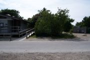 Photo: Buttonwood: Paved road with small gravel parking lot and bathhouse across road, bushes in back ground.