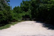 Photo: Buttonwood: Partially shaded gravel campsite with picnic table and grill, bordered by a wood fence and surrounded by bushes.