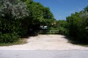 Photo: Buttonwood: Partially shaded gravel campsite with picnic table and grill, backed by a wood fence and surrounded by bushes.