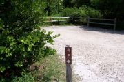 Photo: Buttonwood: Site number post with white number and arrow on a brown background, bushes and site in background