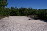 Photo: 075, BAYSIDE: Small gravel campsite with picnic table surrounded by trees.