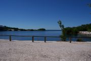 Photo: 075, BAYSIDE: Gravel road with wood fence, boating basin and bushes in the background, cabin on the left.