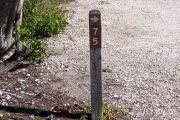 Photo: 075, BAYSIDE: Site number post with white number and arrow on a brown background, bushes in background.