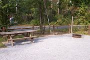 View of a picnic table, fire ring and fence in bright sunshine.