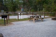 View of a picnic table, fire ring and fence in bright sunshine.