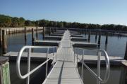 The view from a boat entering the Caladesi marina shows a seawall with a welcome sign in the foreground and docks containing some of the 108 boats slips in the middle. In the distance are a small ticket booth and a picnic pavilion backed by a forest of green cabbage palms.