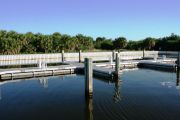 The photograph shows a view of boat slips in the Caladesi Island marina. An aluminum floating dock features power and water pedestals, with an aluminum seawall and green palm trees in the background. Concrete pilings support the docks.  Finger docks protrude out from each side of the main dock at intervals of every two boat slips.