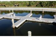 The photograph shows a view of boat slips in the Caladesi Island marina. An aluminum floating dock features power and water pedestals, with an aluminum seawall and green palm trees in the background. Concrete pilings support the docks.  Finger docks protrude out from each side of the main dock at intervals of every two boat slips.