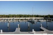 The photograph shows a view of boat slips in the Caladesi Island marina. An aluminum floating dock features power and water pedestals, with an aluminum seawall and green palm trees in the background. Concrete pilings support the docks.  Finger docks protrude out from each side of the main dock at intervals of every two boat slips.