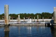 The photograph shows a view of boat slips in the Caladesi Island marina. An aluminum floating dock features power and water pedestals, with an aluminum seawall and green palm trees in the background. Concrete pilings support the docks.  Finger docks protrude out from each side of the main dock at intervals of every two boat slips.