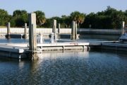 The photograph shows a view of boat slips in the Caladesi Island marina. An aluminum floating dock features power and water pedestals, with an aluminum seawall and green palm trees in the background. Concrete pilings support the docks. Finger docks protrude out from each side of the main dock at intervals of every two boat slips. The photograph shows a view of boat slips in the Caladesi Island marina. An aluminum floating dock features power and water pedestals, with an aluminum seawall and green palm trees in the background. Concrete pilings support the docks. Finger docks protrude out from each side of the main dock at intervals of every two boat slips.