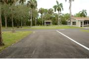 This view shows a wooden picnic table and stand up grill to the right. The water spigot and gray electrical box are to the left. Cabbage Palm is right of the left driveway. Green palms and vegetation are at the back of the site. Site has little shade and usually sunny.