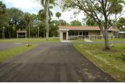 This view shows the ADA wooden picnic table, a water spigot, a stand up grill and gray electrical box. This is an open site with some green vegetation in the background.
