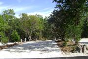 Photo: 018, JOHN PENNEKAMP CORAL REEF SP. Rock with campsite number, partially shaded gravel campsite with picnic table, grill, concrete sewer hookup basin, electric post, and paved road in foreground.