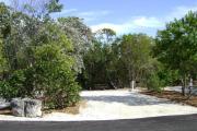 Photo: 020, JOHN PENNEKAMP CORAL REEF SP. Rock with campsite number, relatively no shade gravel campsite with picnic table, grill, concrete sewer hookup basin, electric post, and paved road in foreground.