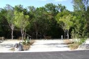 Photo: 025, JOHN PENNEKAMP CORAL REEF SP. Rock with campsite number, almost no shade gravel campsite with picnic table, grill, concrete sewer hookup basin, electric post, and paved road in foreground.