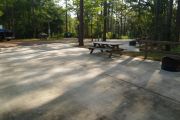 View of ADA-accessible campsite with accessible ground grill, picnic table and concrete pad.