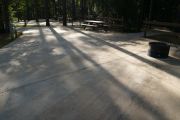 View of ADA-accessible campsite with accessible ground grill, picnic table and concrete pad.