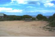 Packed sand campsite with low palmetto plants and sea oats along the back.  The ocean is visible. Picnic table and ground grill off to the left side. Dune crossover walkway to the left with little vegetation. Walkway is non-intrusive.