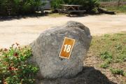 Large rock with metal sign with campsite number 18 on it located to the right of the site. Ground cover around rock.